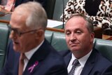 Barnaby Joyce, tight-lipped and staring blankly ahead, sits behind Malcolm Turnbull, who is out of focus in the foreground.