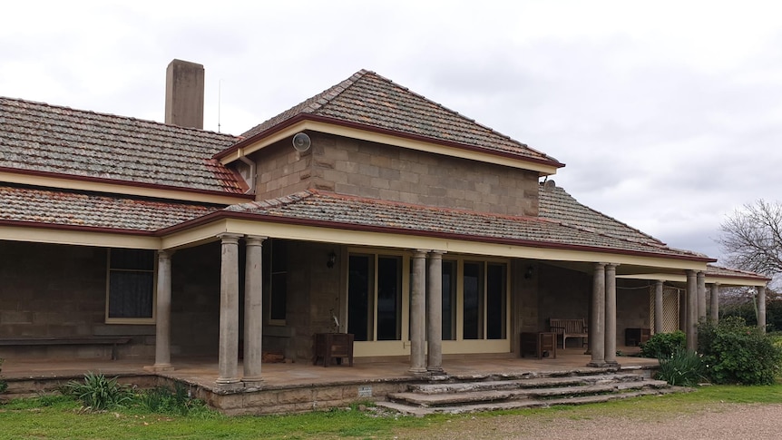 A brick house with pylons and stairs with a gravel path and lawn in front and garden beds.