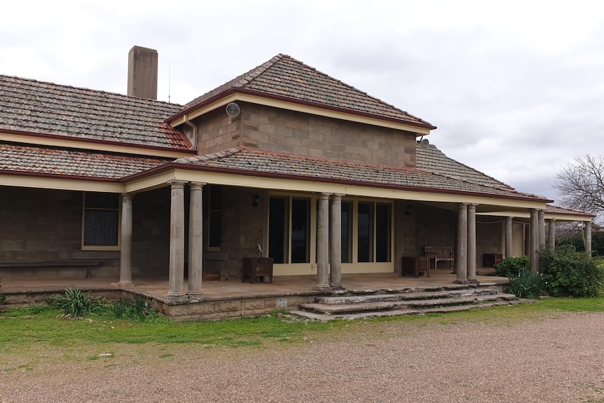 A brick house with pylons and stairs with a gravel path and lawn in front and garden beds.