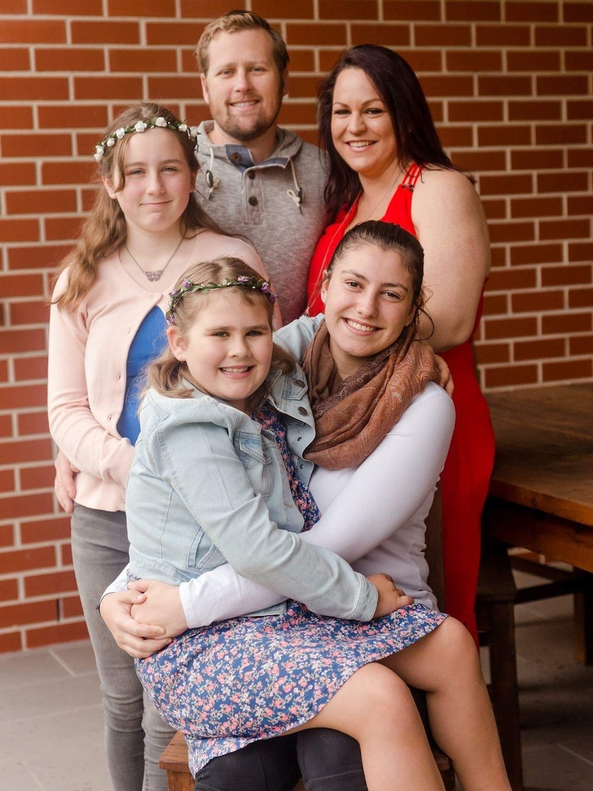 Rachel in a family photo with husband Simon Kunde and her three children. The youngest two kids wear flower crowns.