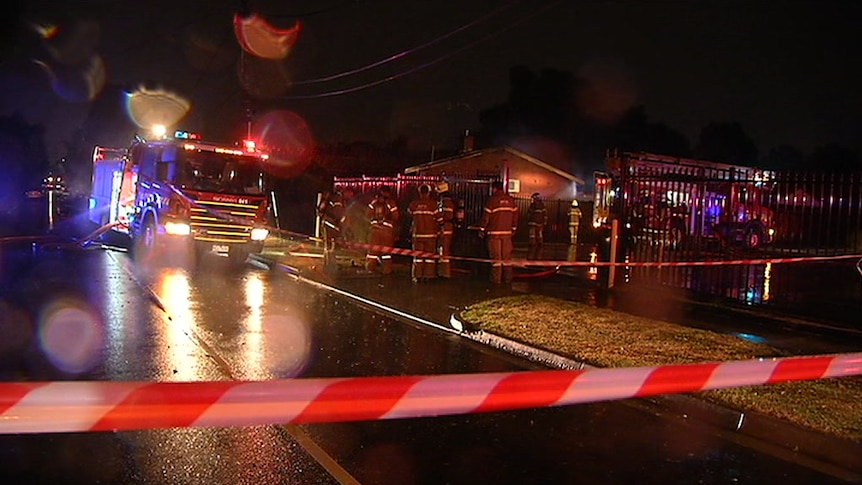Firefighters gather outside a brick home with a fire truck and lights flashing at night.