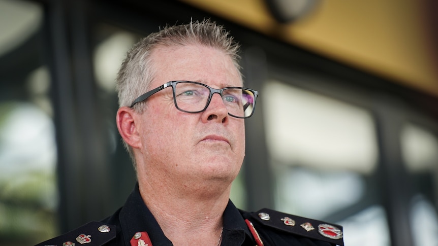 A man with a serious expression wearing black glasses and a navy NT Police uniform looks off camera.