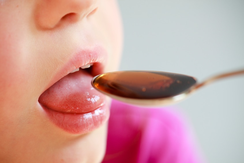 A close up of a child opening mouth to take a liquid medicine from a spoon.