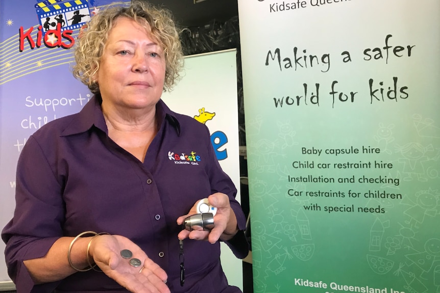 Woman with bobbed curly blonde hair holding button batteries in the palm of her hand