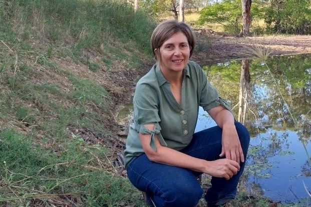 A woman crouches near the edge of a dam.