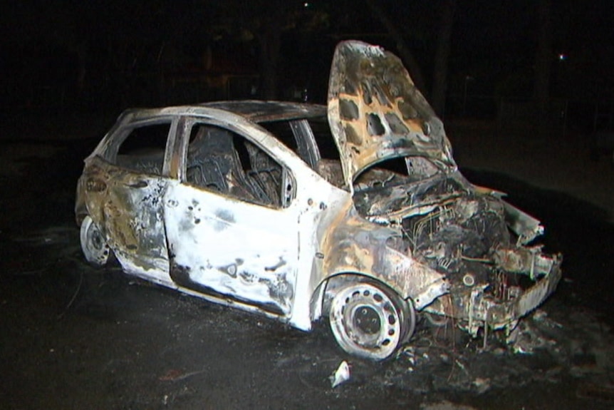 A burnt-out white small car at night