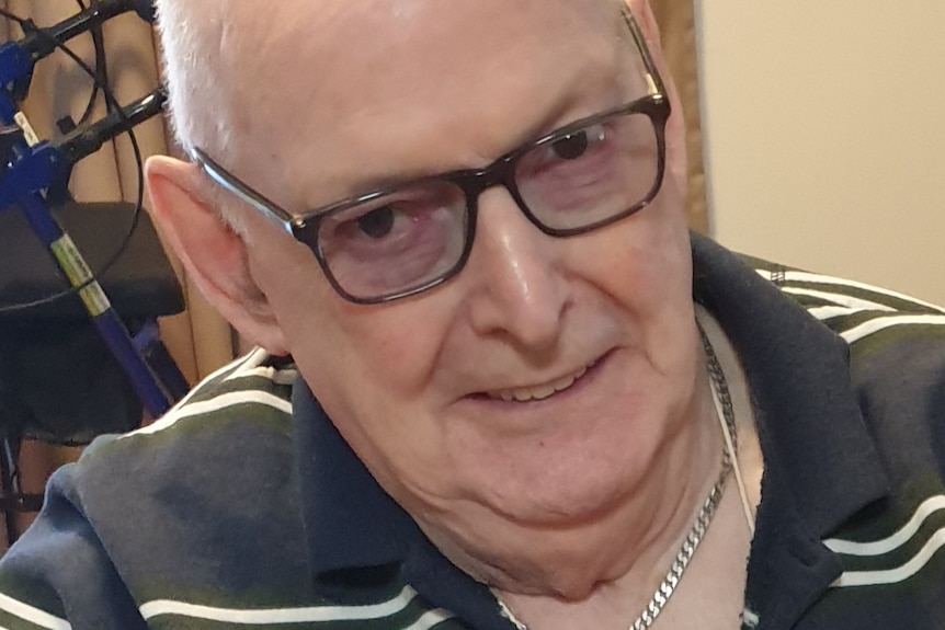 An elderly man wearing glasses smiles.