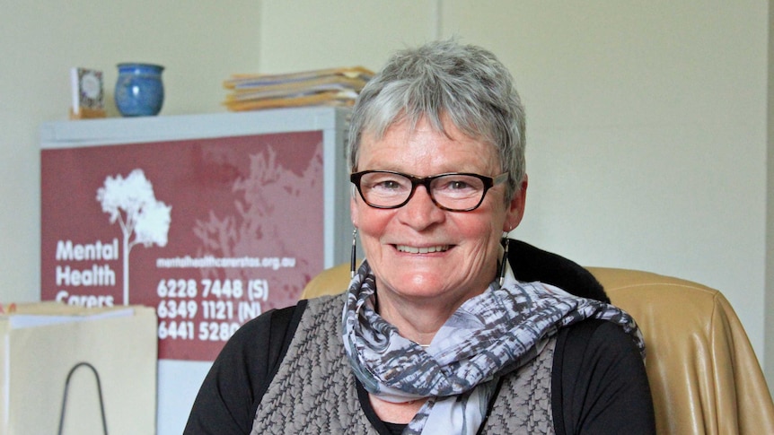 Woman with short grey hair, wearing glasses and a grey patterned scarf smiling