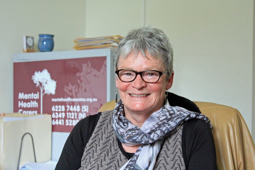 Woman with short grey hair, wearing glasses and a grey patterned scarf smiling