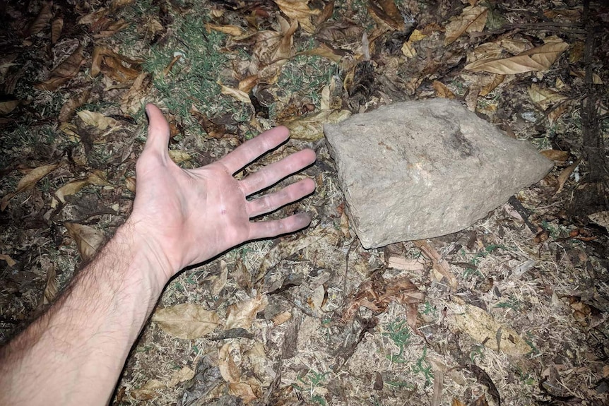 A man's hand and arm beside a large rock