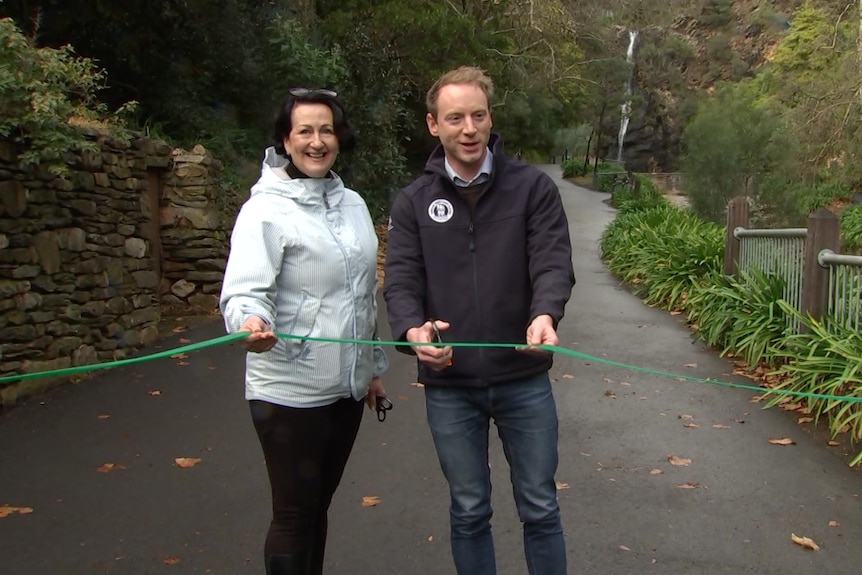 A man and a woman hold scissors to cut a green ribbon across a walking track