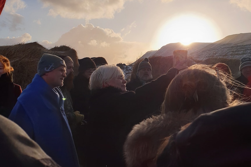 Jóhanna holding bull's horn to sky, surrounded by people.