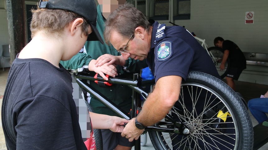 A policeman working on a bike with two boys