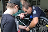 A policeman working on a bike with two boys
