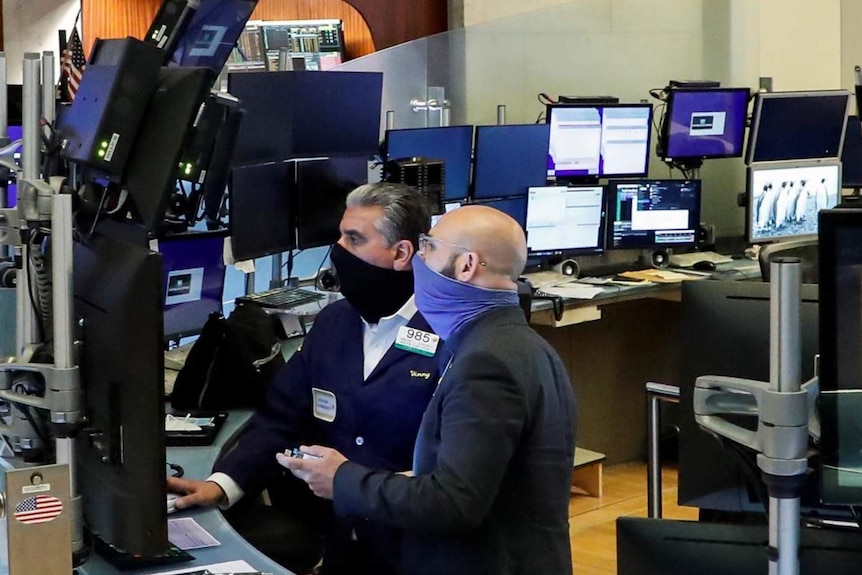 Traders wearing masks at the New York Stock Exchange, surrounded by computer terminals.