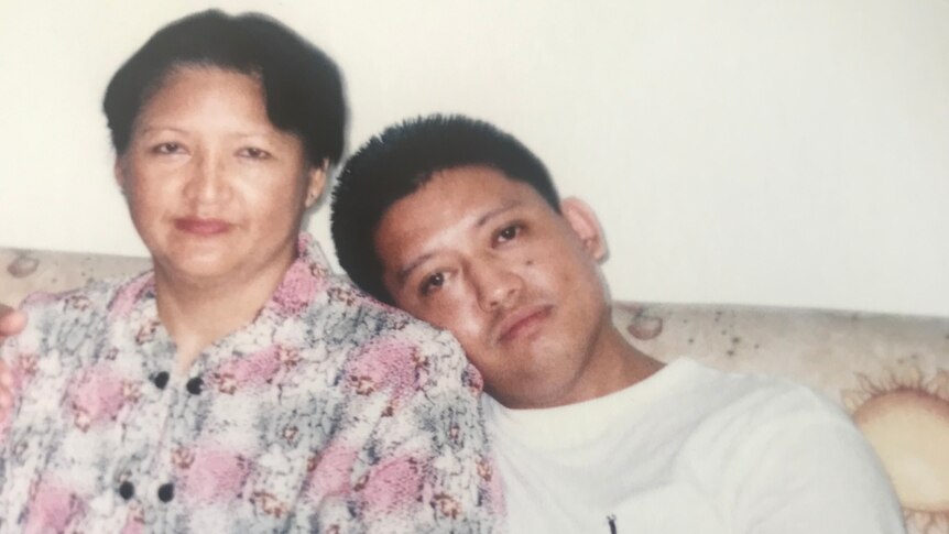 A woman in a floral top sitting next to her son, with his head leaning on her shoulder.
