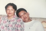 A woman in a floral top sitting next to her son, with his head leaning on her shoulder.