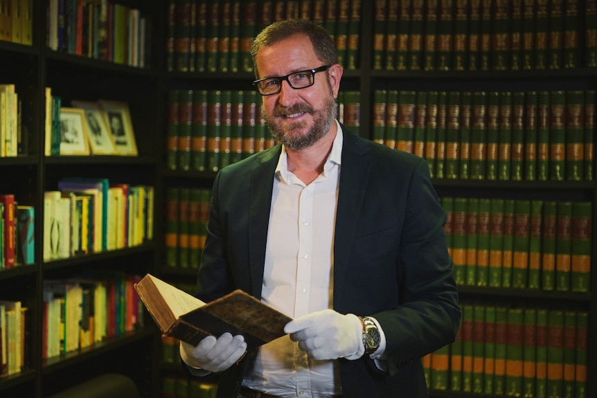 The Fryer Librarian Simon Farley holds a copy of the book wearing a suit and white gloves.