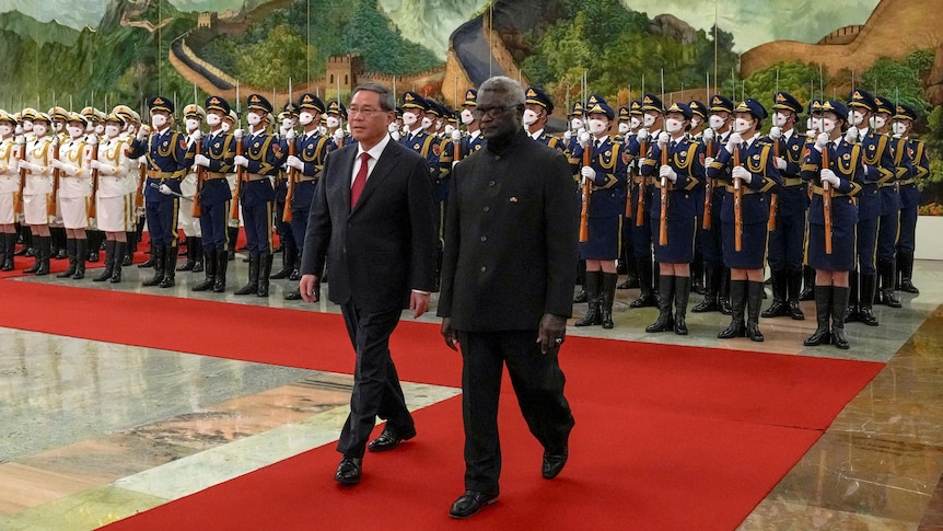 Manasseh Sogavare and Li Qiang review an honor guard during a welcome ceremony as they walk a red carpet.