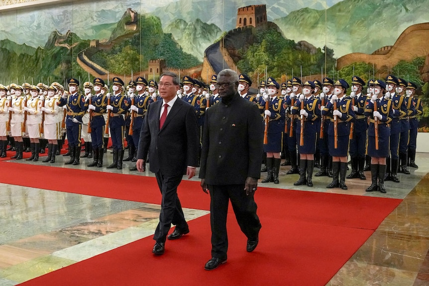 Manasseh Sogavare and Li Qiang review an honor guard during a welcome ceremony as they walk a red carpet.