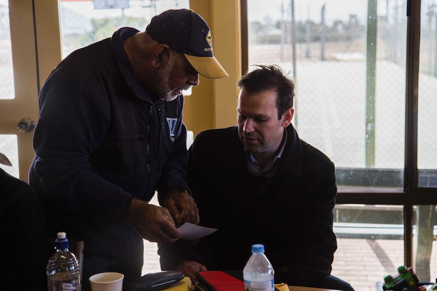 A man stands over Matt Canavan showing him photos in a photo album