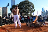 An Indigenous man stands by a fire at Federation Square, while people watch on.