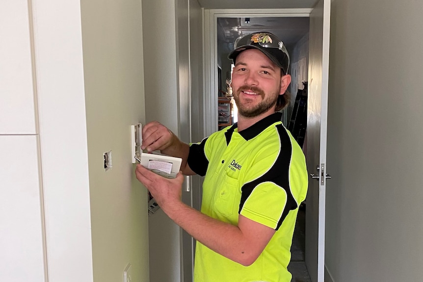 A man in a cap wearing high vis work clothes smiling at the camera while working