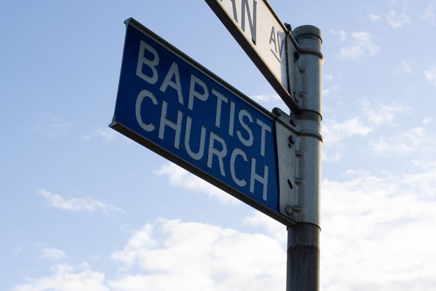 A blue road sign that says BAPTIST CHURCH with blue sky behind it