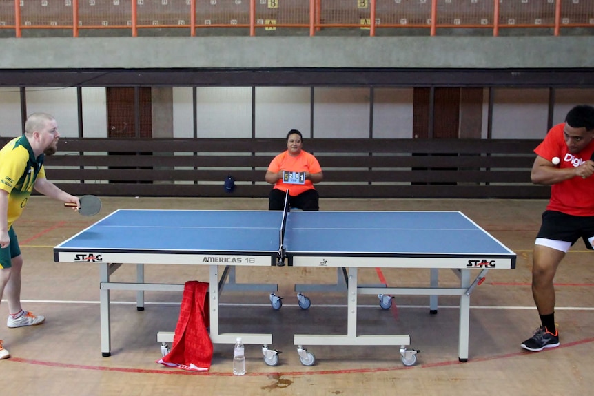 A side-on-view of a table tennis table with Trevor on the left in his Australian colours competing with a Tongan player in red