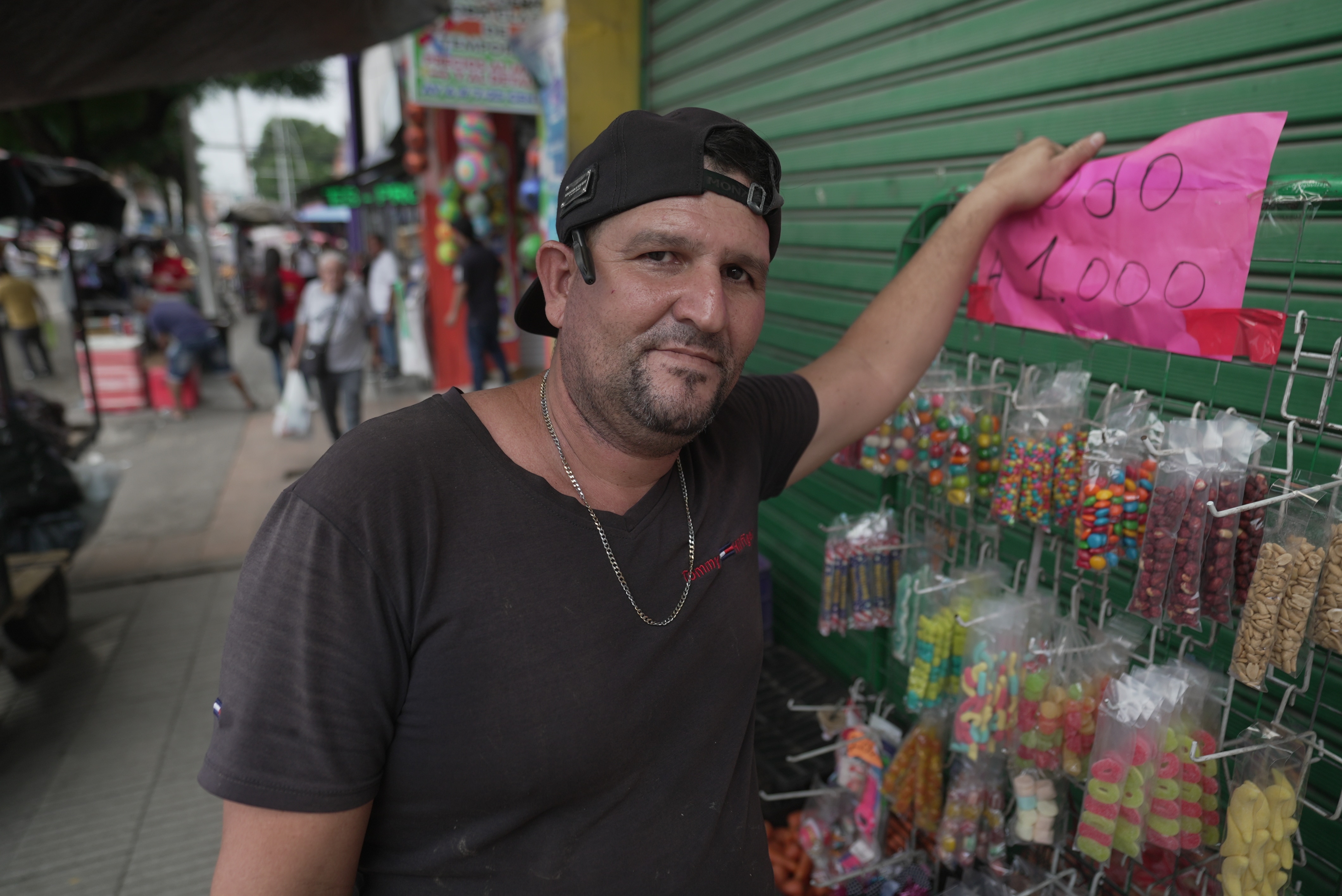 Homem parado em frente a uma banca de mercado vendendo doces. 