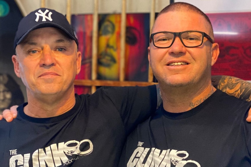Two men stand wearing The Clink t-shirts