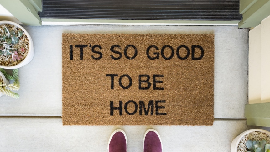 A person stands in front of a welcome mat that says "it's so good to be home".