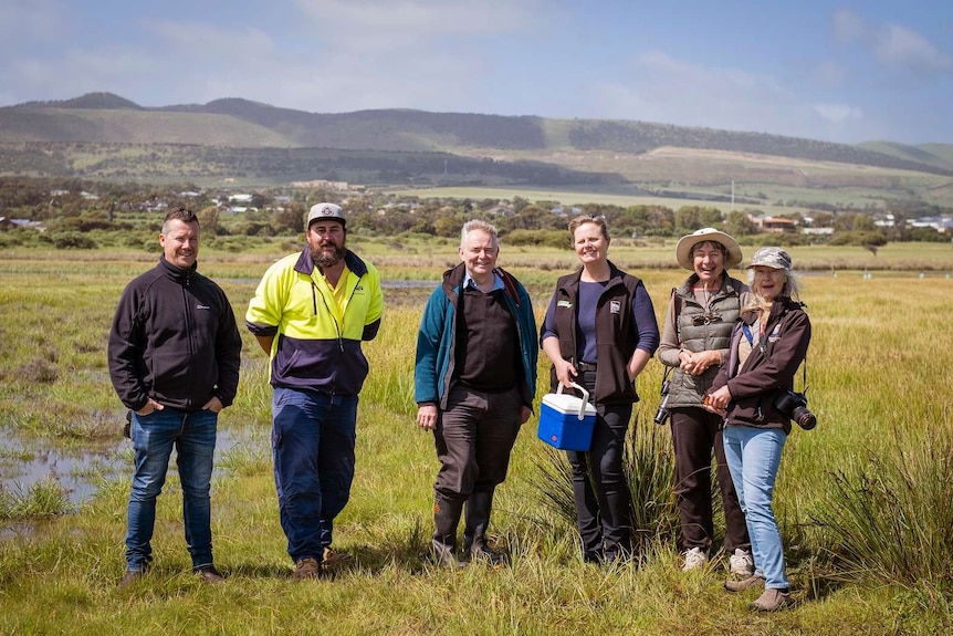 A group of people in grass and puddles with a range of hills behind