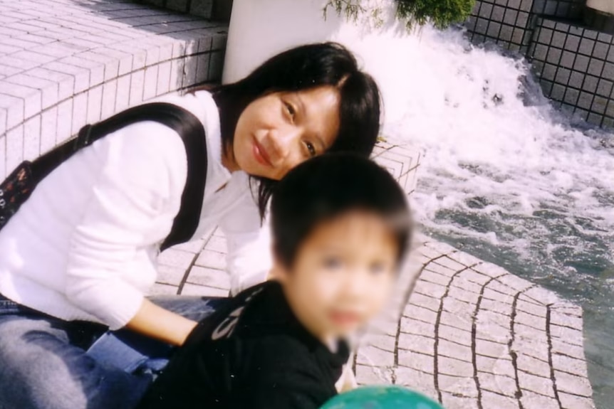 A young boy near a water fountain with his mother.