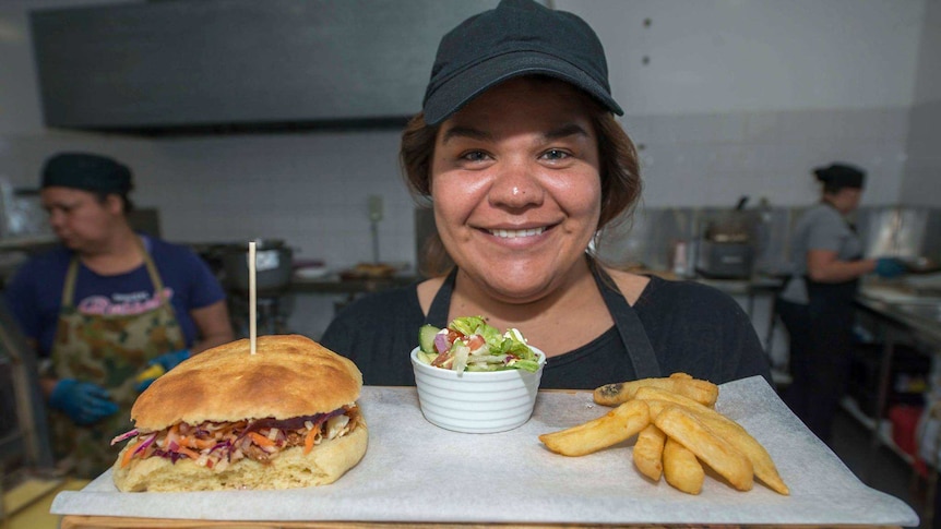 A young woman holds up a tray containing a hamburger, chips and salad