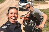 A surprised looking female police officer points at a smiling young man who is holding a bike