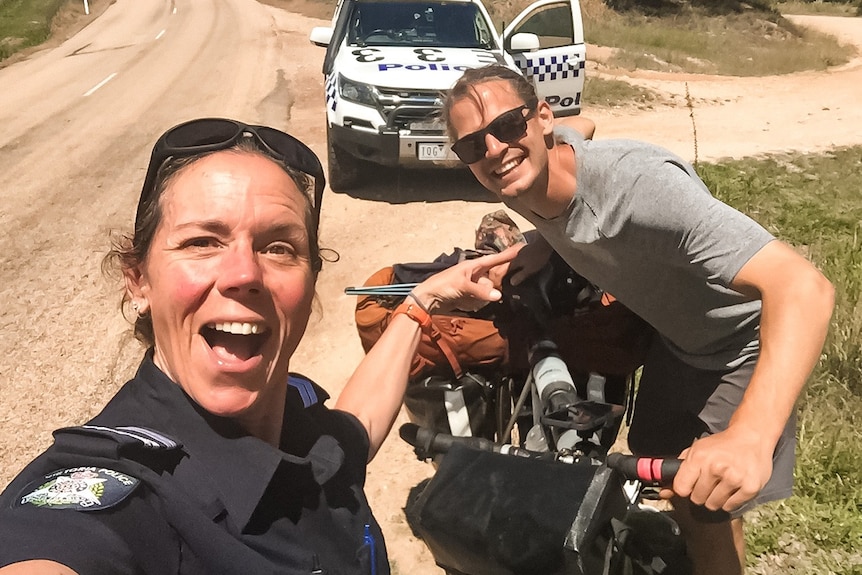 A surprised looking female police officer points at a smiling young man who is holding a bike