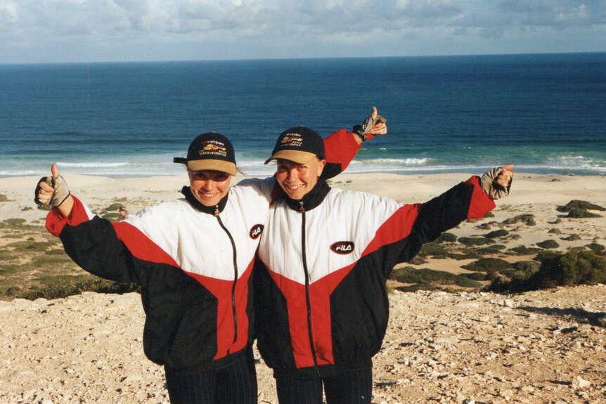 Two women stand on the beach in matching track pants and hats