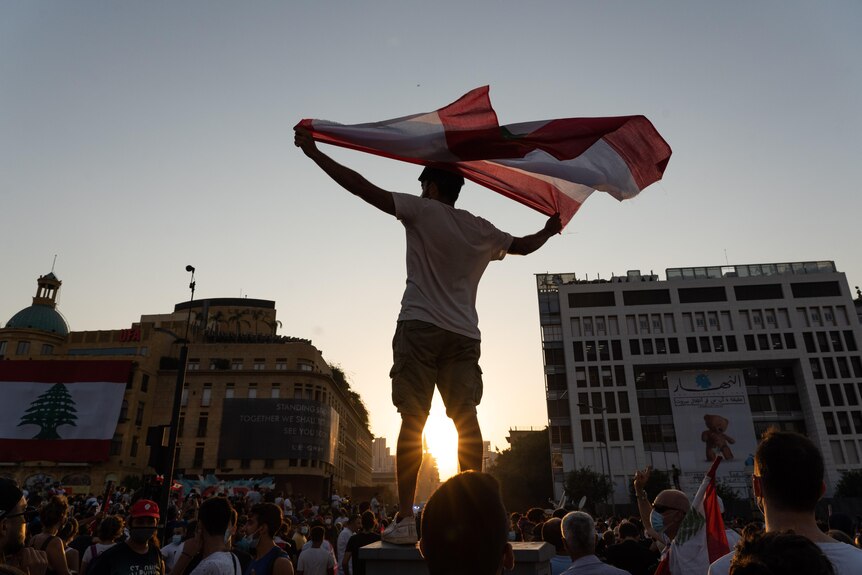 A silhouette against the sky of a man holding a flag above a crowd of people.   
