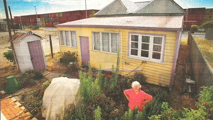 Carmel Mullally stands outside her yellow weathered cottage sandwiched between port infrastructure at Fremantle Port