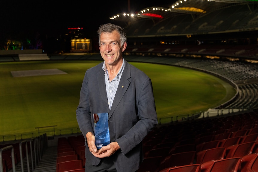 A man posing with a glass award in the stands of an oval