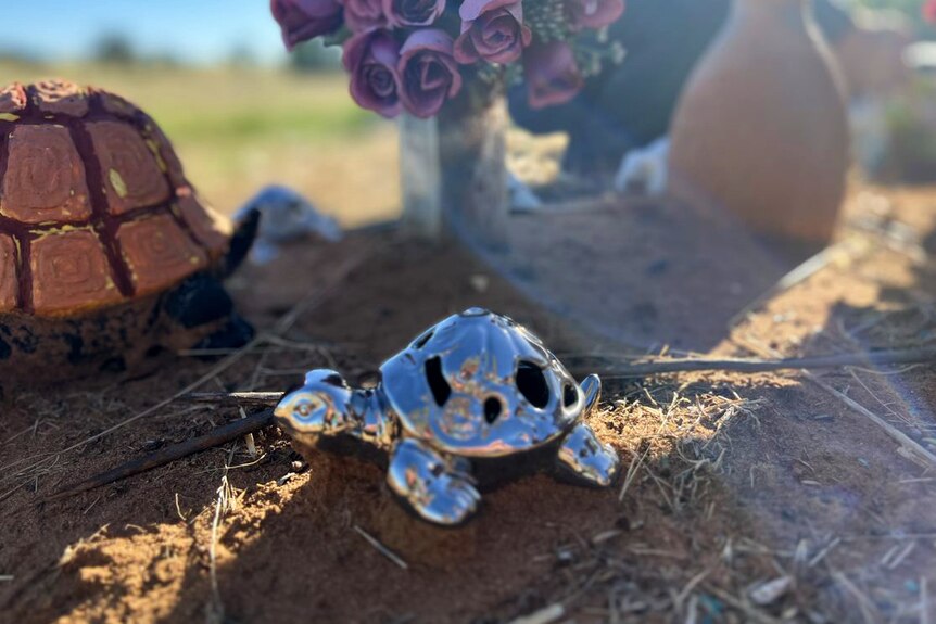 A silver turtle statue sits around flowers and other tributes.