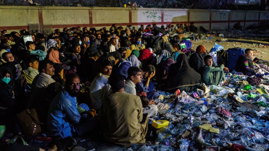 crowd of refugees in kabul sitting tightly packed together on the ground surrounded by debris
