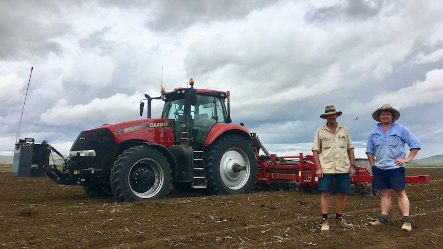 Two male farmers stand in front of a planter in the paddock