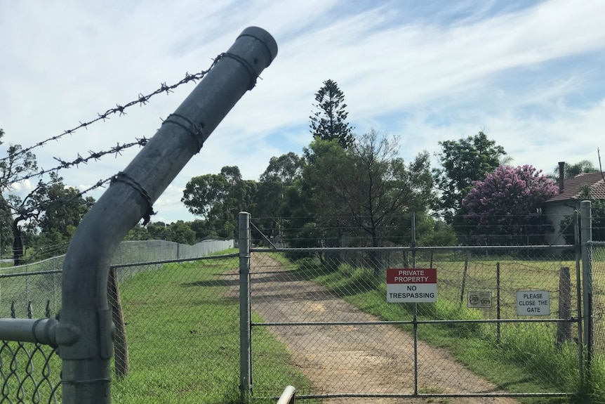 A chain link fence and gate surrounded by a tall barbed wire fence. A sign on the gate says "no trespassing'.