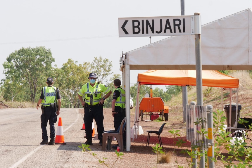 Police stand under a gazebo near a street sign pointing to Binjari