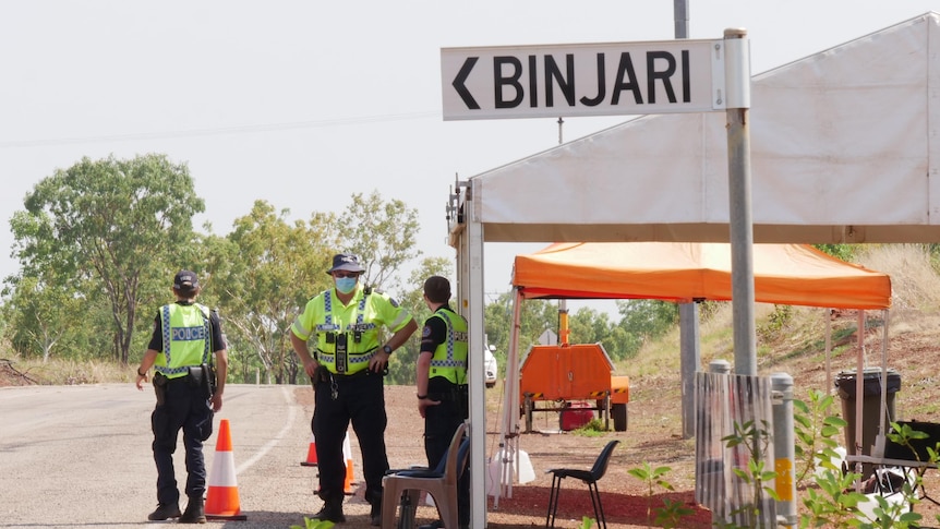 Police stand under a gazebo near a street sign pointing to Binjari