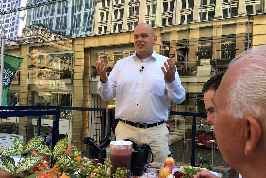 Edwin Van Raalte from RaboDirect in Martin Place, surrounded by buildings, addressing a table of journalists about food waste.
