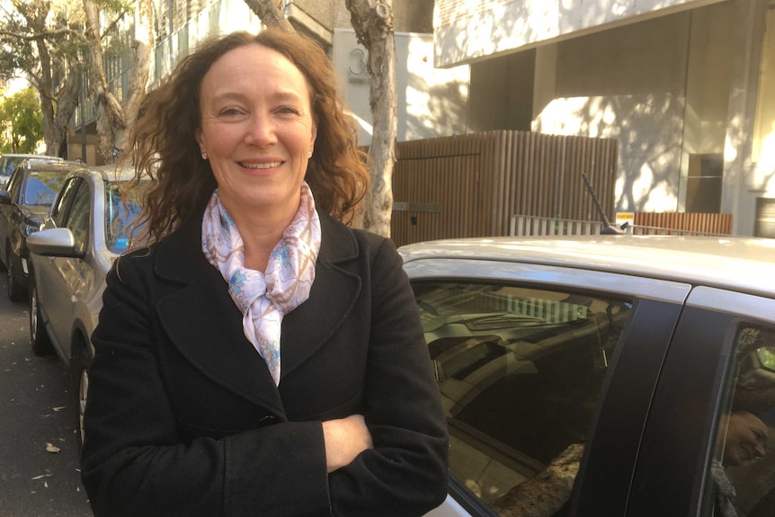 A woman with her arms crossed standing in front of parked cars.