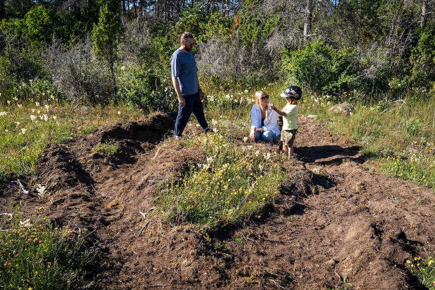 A young family inspects thought tracks on a grassy field near their home.